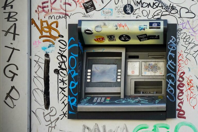 An ATM embedded in a graffiti-covered wall, showcasing vibrant street art in a city setting.