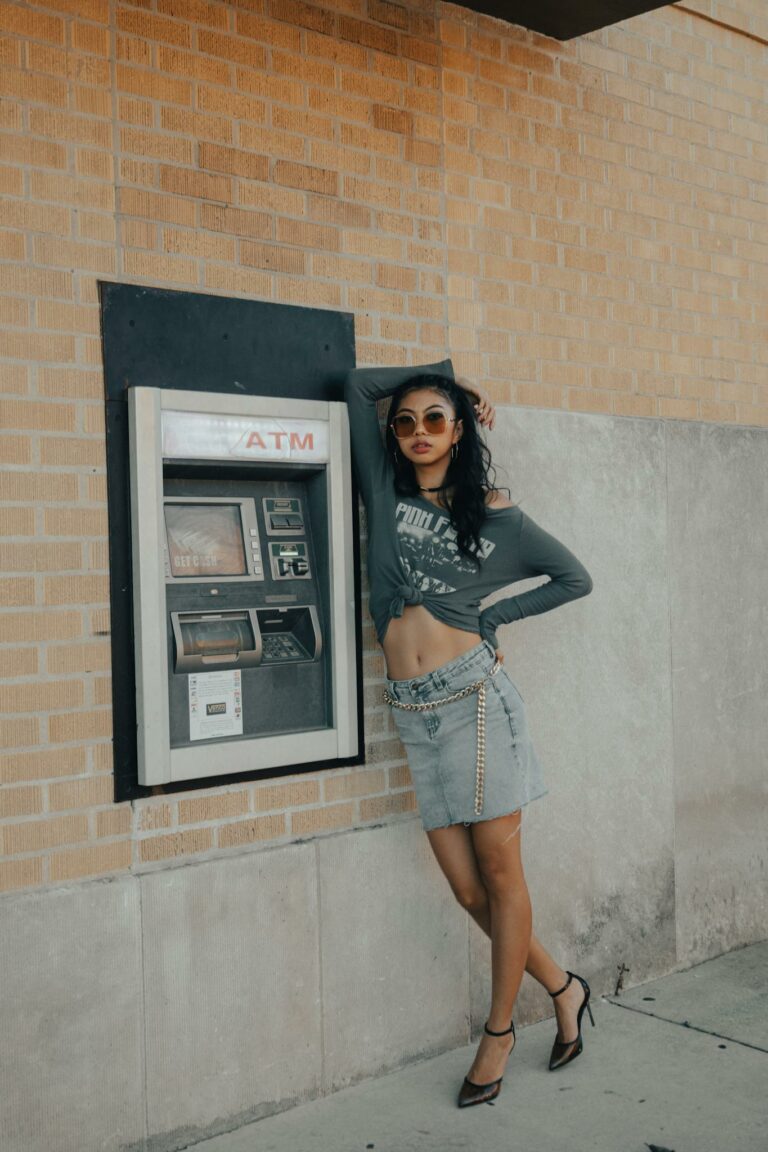 Fashionable woman leans against an ATM, showcasing urban style and confidence.